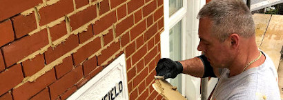 picture of brick restoration company employee during repointing red brickwall in london
